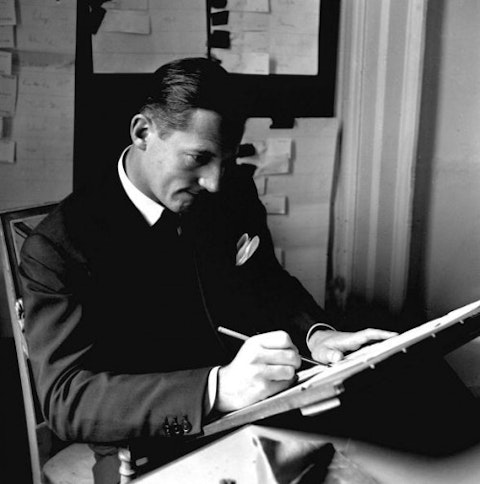 1952. Hardy Amies, famous London Courturier designs "Amoroso", his material board in the background. At this board on which are pieces of materials from all over the world. here he is pictured working on his collection for next season.