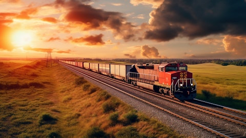 A freight train moving through a rural landscape, its engine and numerous rail cars carrying the company's cargo.