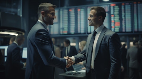 A businessman in the foreground shaking hands with a colleague in a trading floor.