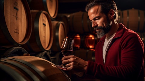 A winemaker examining a glass of red wine from a barrel in a cellar.