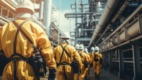 A line of workers in a refinery wearing protective suits and masks, overseeing the production process of specialty gases.