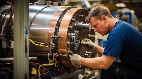 A man in overalls soldering a large water heater inside a manufacturing facility.