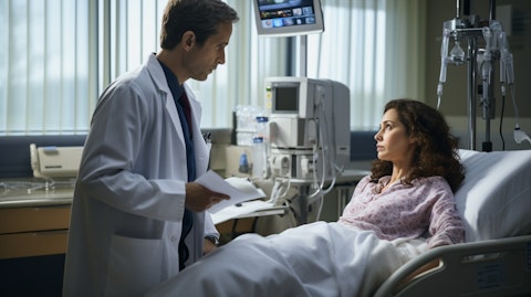 A doctor speaking with a patient in a hospital bed in an exam room.