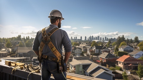 A construction worker standing on a rooftop with a toolbelt in hand, looking out at a new home development in the background.