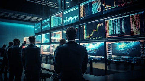 A row of traders in a trading room monitoring stock market prices with a large digital screen in the background.