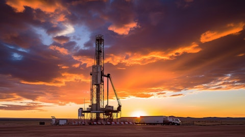 A drilling rig on a remote oilfield, its tower silhouetted against a setting sunset.