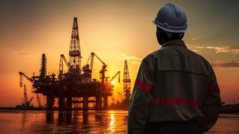 A worker in a hard hat looking up at an offshore drilling rig at sunset.