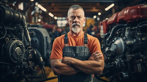 A mechanic standing proudly in a factory floor surrounded by the engines the company produces.