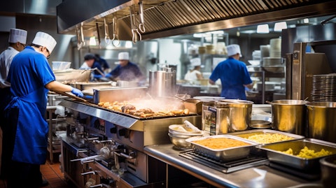 A professional kitchen bustling with activity, utilizing different pieces of Kitchen Equipment, such as Conveyor Ovens, Fryers, Steam Cookers and Warming Equipment.