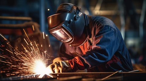 A worker in safety gear welding a complex titanium component in a factory setting.