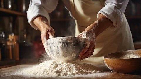 A close up of a baker stirring a bowl of flour and sugar in a bakery.