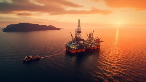 Aerial view of a oil rig in the middle of an ocean, with a bright orange sunrise in the background.