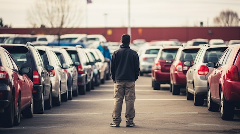 A row of used cars with shoppers inspecting them on a lot.
