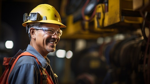 A portrait of an industrial worker wearing safety equipment, smiling while inspecting a piece of equipment.