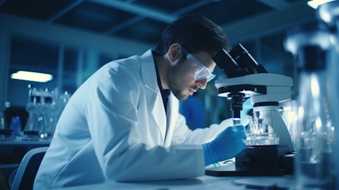 A scientist in a lab coat holding a vial while examining a microscope in a biotechnology lab.