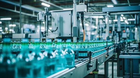 A factory floor with industrial line machinery operating, producing glass containers.