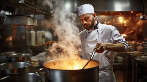 An experienced cook stirring a large pot of soup in a commercial kitchen.