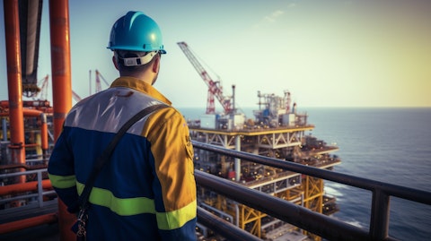 A worker in a hardhat and safety vest standing atop an offshore drilling rig, overlooking the sea.
