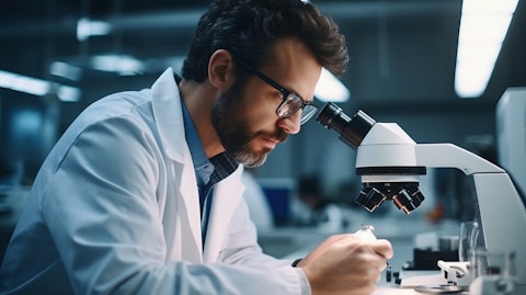 An ophthalmologist in their office wearing a lab coat and looking through a microscope at a contact lens.