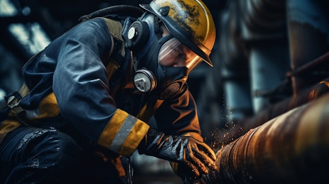 A person wearing protective gear and a respirator, inspecting a corroded pipe in a refinery.
