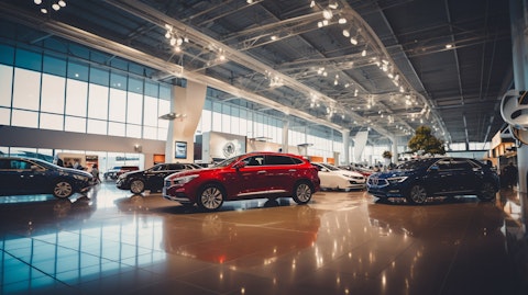 A wide view of a large auto dealership, its showroom packed with different types of cars.