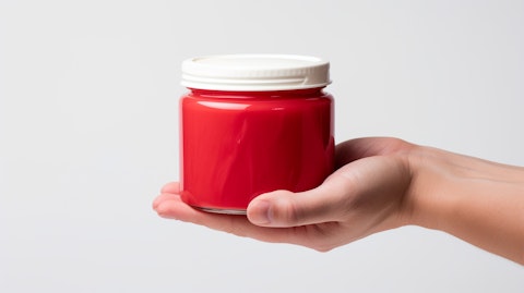 A hand holding a bright red jar of mayonnaise against a white studio background, reflecting the company's range of products.