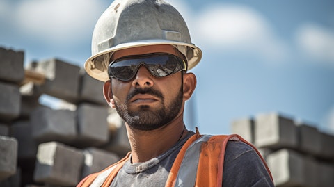 A construction worker wearing a hard hat and safety glasses at a site, carrying concrete blocks.