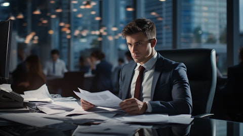A business executive in a suit working at their desk, surrounded by a busy office environment.