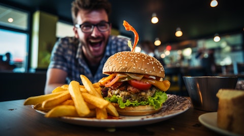A customer biting into a freshly prepared char-grilled burger, with crinkle-cut French fries and a chopped salad in the background.