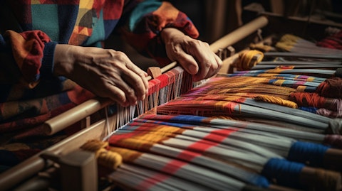 A close-up of a worker's hands using a loom to craft textile materials.