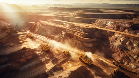 An aerial view of a large open-pit mine at sunrise, with trucks driving in its depths.