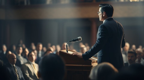 A business executive confidently giving a speech in front of a boardroom of attendees.