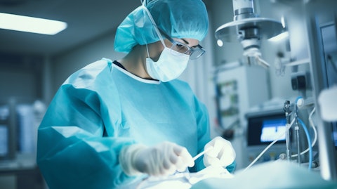 A healthcare professional wearing a face mask and surgical gloves operating a medical device in a clinical setting.