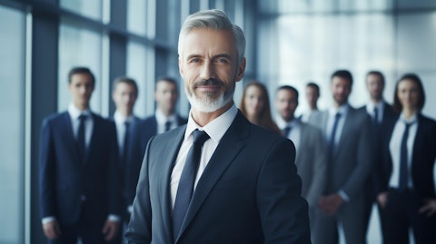An executive in a suit flanked by workers, all smiling and looking confident.