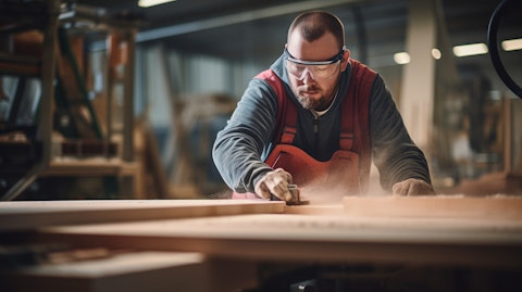 A craftsman building cabinets in a factory wearing safety glasses and protective gloves.
