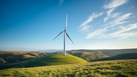 A wind turbine on a hilltop, surrounded by grass and blue sky.