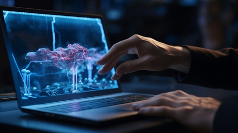 A close-up view of a scientist's hand pressing keys on a laptop as another looks closely at a 3-D model on a large monitor.