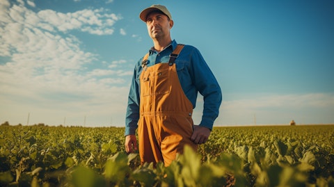 A farmer in boots, overalls and a wide brimmed hat, proudly standing in a field of soybeans and yellow peas.