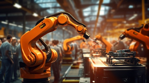 A robotic arm working on a manufacturing line in sharp focus, with a blurred human arm controlling it in the background.