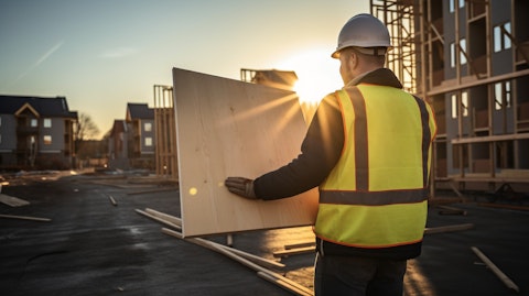 An engineer carrying a housing panel for a modular building across a construction site.