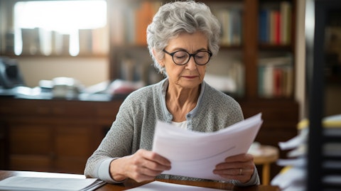 An older woman, seated at a desk, reviewing the documents of a healthcare program.