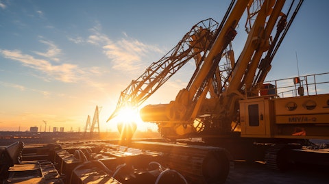 A close-up of a large crawler-mounted lattice-boom crane with the sun in the background.