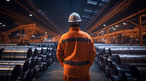 A steel worker in high-visibility gear standing in front of a vast array of steel products.