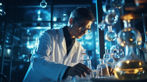 Close up of a chemist in a lab coat holding a beaker, surrounded by sophisticated life science equipment.