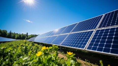 A photovoltaic solar module array with a clear blue sky overhead and a hint of green foliage in the backdrop.
