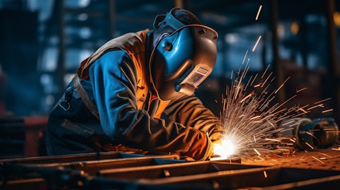 A close-up shot of a worker welding steel beam together in a large steel foundry.
