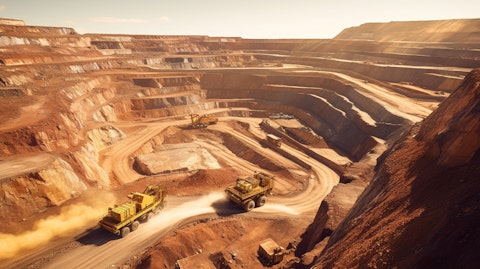 Aerial view of a large open-pit gold mine with a fleet of mining trucks in the foreground.