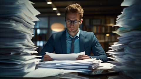 A business person looking over a stack of business documents, analyzing results with a laptop.