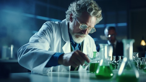 A close up of a chemist in a laboratory, pouring liquid from one beaker to another.