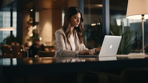 A woman in business attire and a laptop typing away in a modern office workspace.